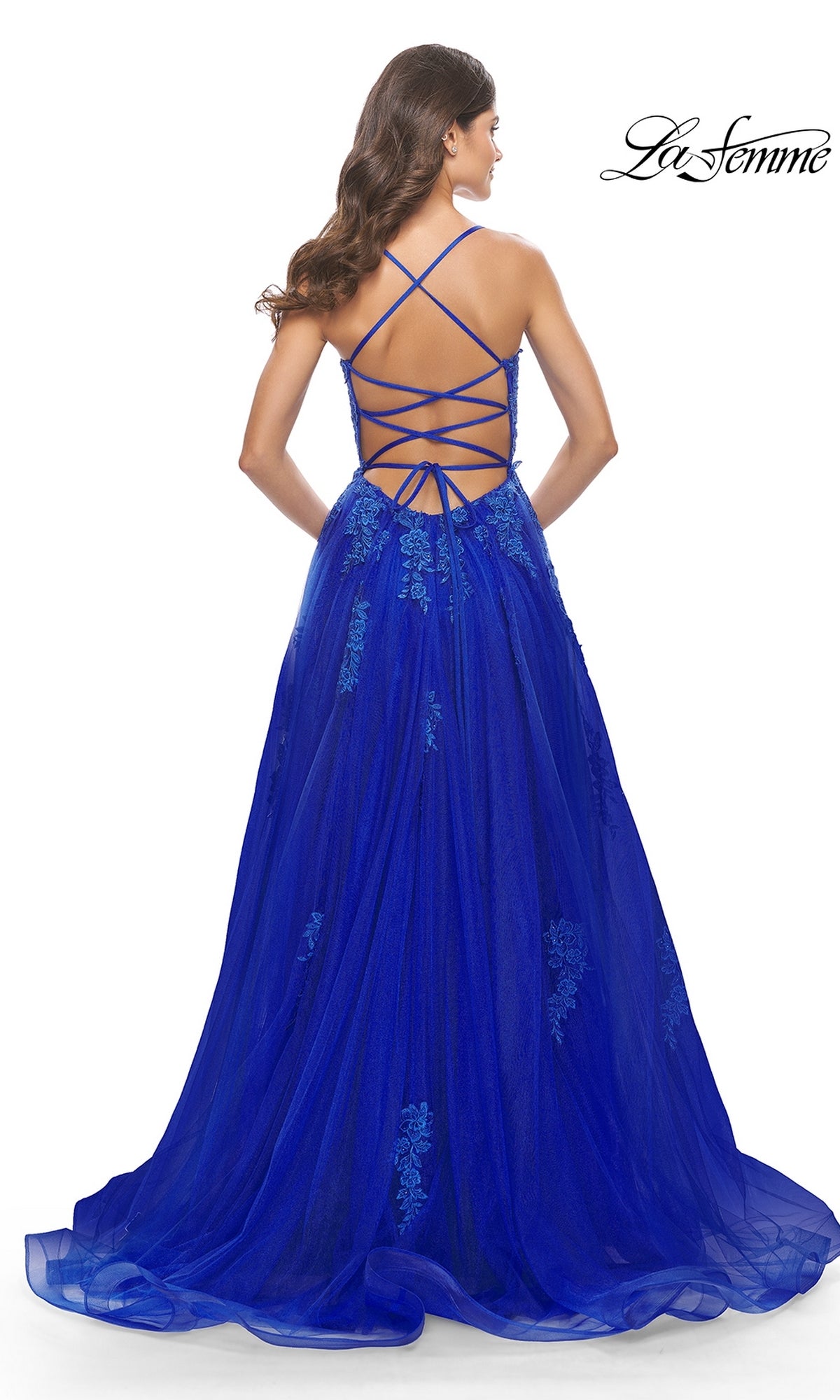 A woman stands with her back to the camera in the La Femme Long A-Line Lace Prom Ball Gown 31135, featuring royal blue embroidery, a crisscross open back, and a flowing skirt.